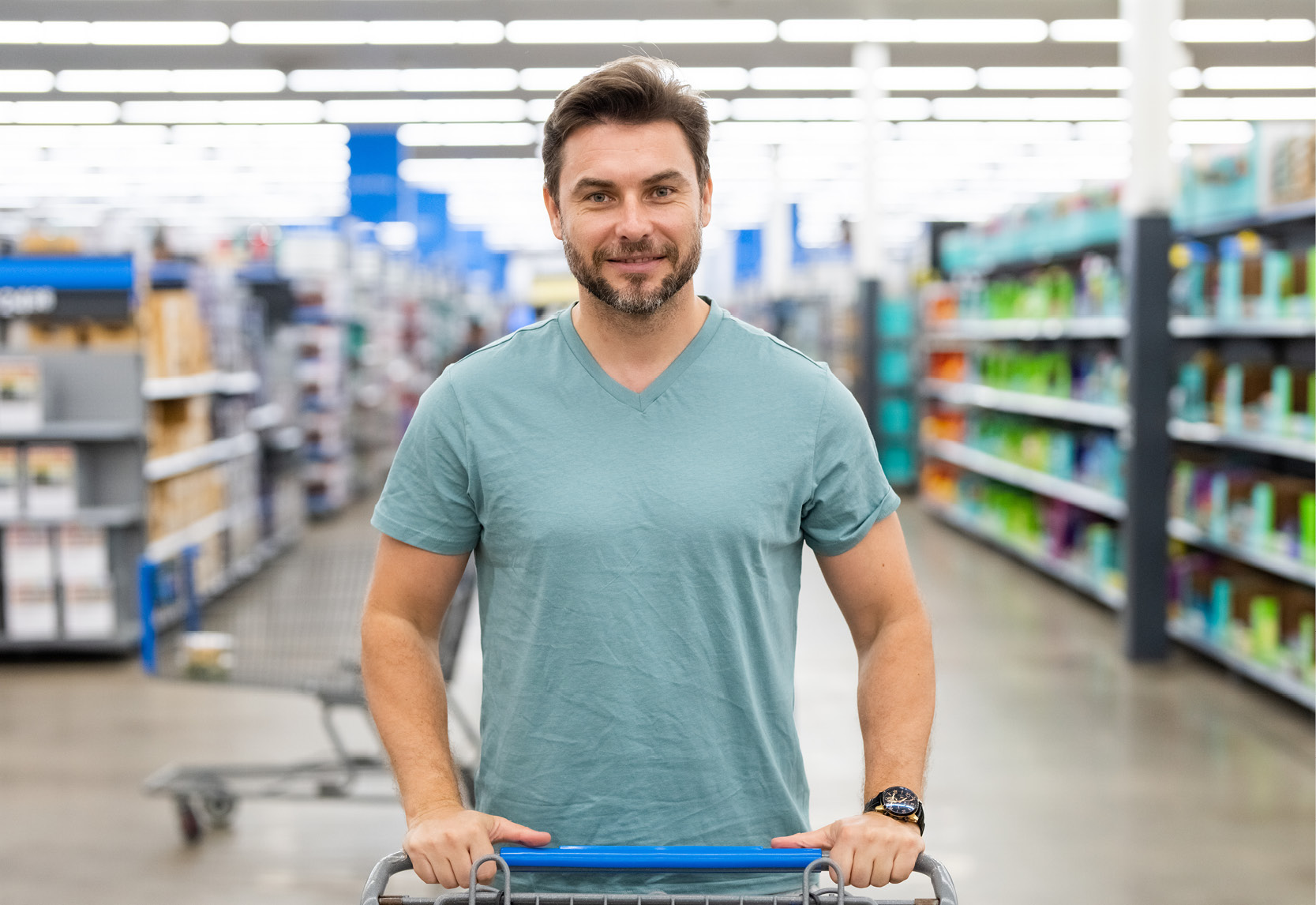 Un homme en T-shirt pousse un caddie dans un magasin aux rayons pleins.